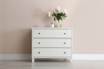 White chest of drawers with bouquet and candle near beige wall - obrazy, fototapety, plakaty