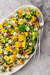 Salad with young corn and cheese, onion and broccoli with dill and parsley, fresh summer salad in an oval dish, top view