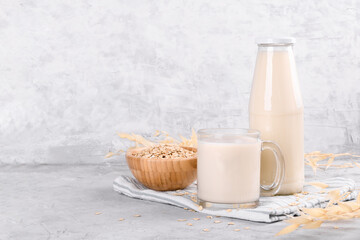 Vegan non dairy alternative milk. Oat milk in a mug, in a bottle and a bowl with oat flake on grey stone table, copy space