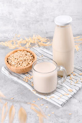 Vegan non dairy alternative milk. Oat milk in a mug, in a bottle and a bowl with oat flake on grey stone table, copy space