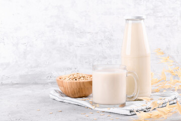 Vegan non dairy alternative milk. Oat milk in the bottle and in the mug with oat cereal flake on grey stone table
