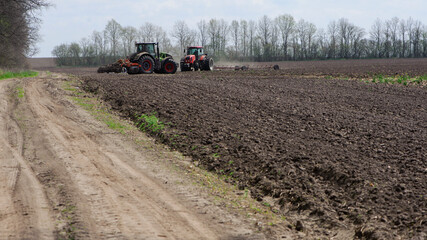 Fototapeta premium two red tractors, work in the field on a large tractor, harvesting, farming. two red tractors in a field in summer during an agricultural exhibition. Ukraine, Kiev region
