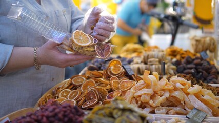 Close up of salesman in a disposable glove packing dried fruits to the plastic box at the outdoor market 