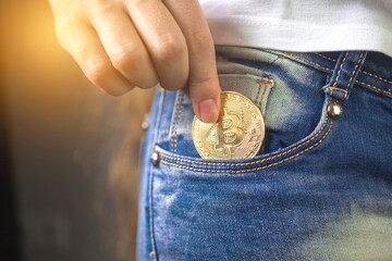 Close-up of woman putting bitcoin in jeans pocket, golden cryptocurrency coin in pocket background...