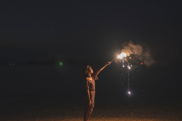 夕暮れの海で花火をする女性