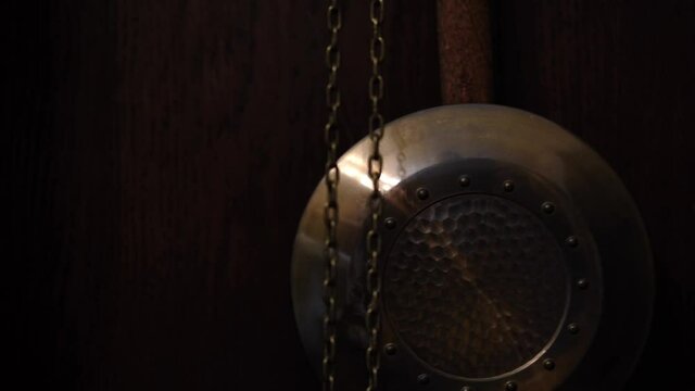 Pendulum of the old clock through the blurry image of the chains. Close-up. Selective focus