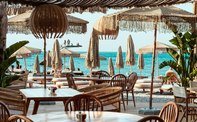 Beach  club view, modern white sun beds, knitted makrome umbrellas for sun protection, sea on...