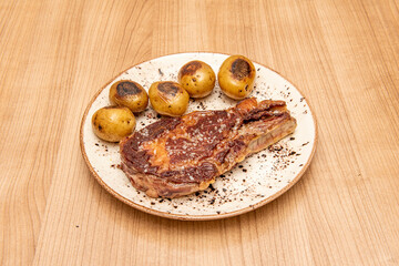 Super entrecote with sea salt and seasonal potatoes or cachelos on a white plate and wooden table