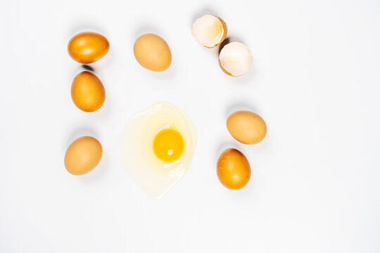 Top view image of raw eggs and one of them broken showing yolk and white on white background
