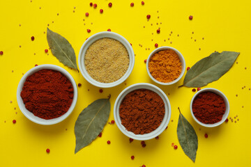 Different spices in white bowls on yellow background
