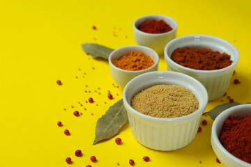 Different spices in white bowls on yellow background
