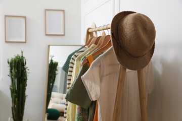 Fototapeta na wymiar Rack with hanging clothes and straw hat indoors. Interior design