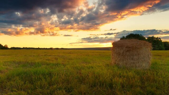 Time lapse of haystack at Sunset. Beautiful summer landscape with cloudy sky and field with haystack.