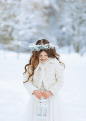Fototapeta na wymiar Little girl enjoys the snowfall. Little girl in a wreath holding a Christmas lantern in her hands. Christmas background.