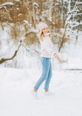 Amazing girl in a Winter Suede Lambs Wool Jacket enjoying winter moments. Outdoors photo of blonde in a pink hat having fun on a snowy morning on a blurred nature background.