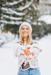 Smiling woman demonstrates her bouquet of dried flowers on a background of winter park.