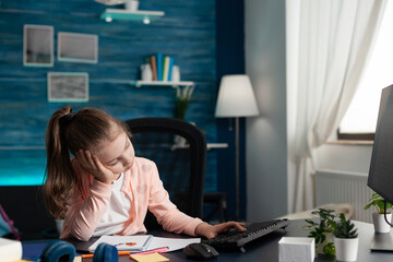Smart pupil feeling sad and bored of online school classes and lessons at home. Portrait of stressed child doing homework for elementary educational knowledge in internet classroom