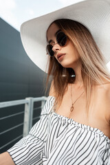 Summer portrait beautiful young woman in sunglasses in dress in straw hat in city on summer day....