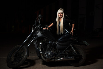 Fototapeta na wymiar Sexy biker girl is posing on motorcycle in the night. She is happy looking at camera.