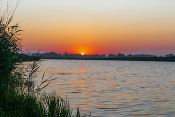 Obraz premium Beautiful sunrise on a forest lake. There are two boats with fishermen on the water in the predawn darkness.