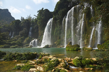 Big waterfall Ban Gioc among trees and mountains on a sunny summer day