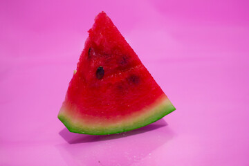 A triangular slice of red watermelon on a pink stink. 