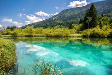 Beautiful landscape of Jasna artificial lake surrounded by forest and people enjoying surfing on a sunny day in kranjska Gora - Slovenia