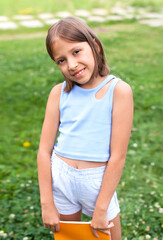 A little girl is reading on the grass. She has an expression of pleasure on her face, and she looks very relaxed. There is quite a lot of open space around it.