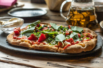 Roman pizza margarita with pesto sauce and basil. Side view on a black plate. Wooden background.