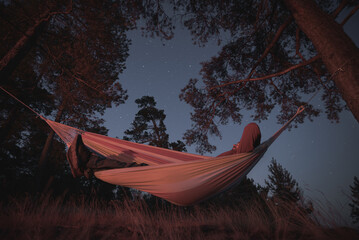 A man sleeps in a hammock on a starry night. Campfire lighting