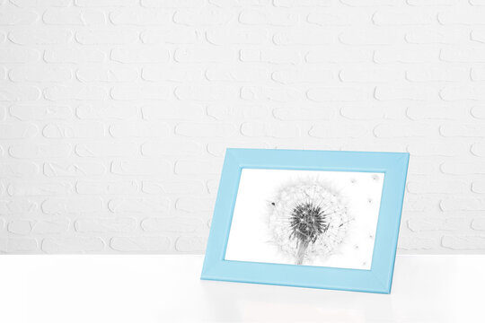 Light blue color photo frame with dandelion picture at white bricks wall