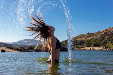 Young woman in a bikini doing a wave with her hair in a lake. Summer. Movement concept. Copy space. Selective focus.