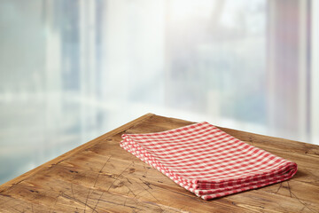 Empty wooden table with red checked tablecloth over  blurred window background.  Kitchen mock up...