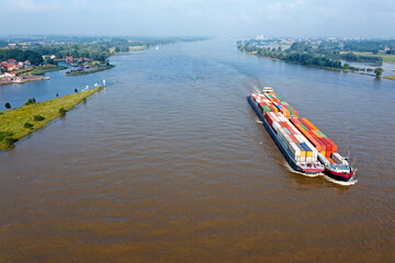 Obraz premium Aerial from a freighter full of containers cruising on the river Merwede near Gorinchem in the Netherlands in a flooded landscape