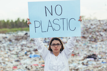 Female volunteer pickets a landfill with a poster no plastic, activist struggles with environmental...