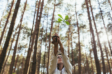 Young female volunteer plants a forest, holding an oak tree seedling in her hands