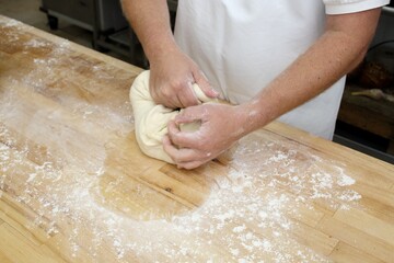 Closeup of baker kneading dough on wooden table