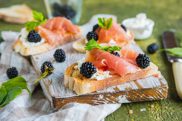 Snack, open sandwich with prosciutto, cream cheese and fresh blackberries on a wooden board on a green concrete background. Sandwich recipes.