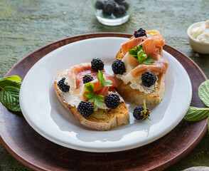Snack, open sandwich with prosciutto, cream cheese and fresh blackberries on a white plate on a green concrete background. Sandwich recipes.
