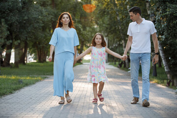 Family - mom, dad and daughter are walking along the pavement in the city summer park.
