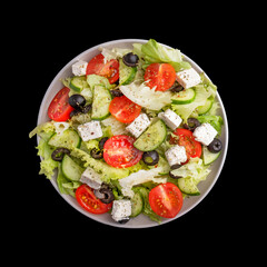 Vegetable salad isolated on a black. Cherry tomatoes, cucumbers, feta cheese, balck olives and lettuce on a plate. Top view