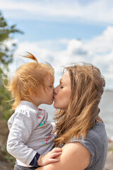 Mom with a little daughter in her arms kissing on the beach