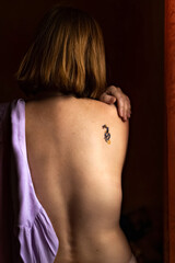 Naklejka premium The naked back of a young woman with red hair and a tattoo on her shoulder