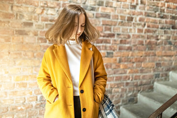 Portrait of a young woman in a bright yellow coat against the background of a brick wall by the window.In the sunshine.