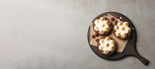 Delicious salted caramel chocolate tarts with meringue and hazelnuts on grey table, top view. Space for text