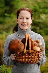 A happy woman with a basket of mushrooms in the forest. Portrait of a forester with a harvest.