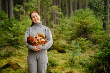 Young woman happily holds a wicker basket with edible mushrooms against the background of a green forest. © vadimverenitsyn