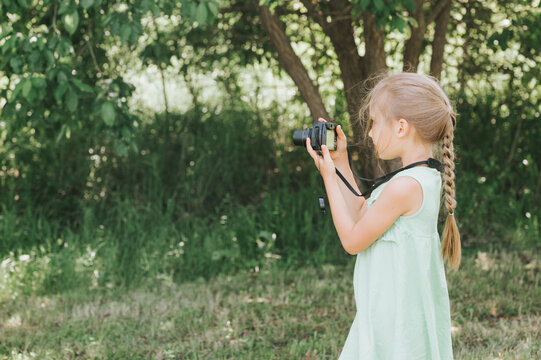 a happy little seven year old kid girl photographs a summer natural landscape with a camera using live view. children adopt their parents hobbies. summer children's education on vacation