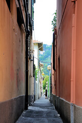 Fototapeta na wymiar A narrow passage between houses with bright orange walls in a southern European city. A woman in a black dress is standing on the path.