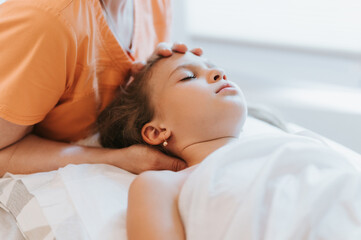 Obraz na płótnie Canvas real doctor osteopath hands does physiological and emotional therapy for eight year old kid girl. pediatric osteopathy treatment session. alternative medicine. taking care of the child's health